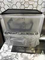 Two stacked translucent rectangular Tupperware containers with black lids, one lid showing the Tupperware logo embossed, photographed on a marble and tiled surface.