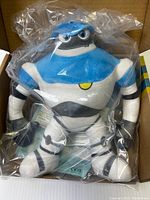 Blue, white, and black plush robot figure in plastic inside the box