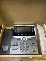 Cisco IP phone in open box showing handset and keypad.