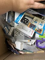 Top view of box showing assorted electronic accessories including packaged phone case, battery sleeves, power adapter, assorted cables