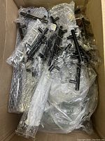Box filled with multiple packaged black metal cabinet handles and other hardware items wrapped in bubble wrap and plastic.