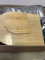 Box with wooden cutting board and smaller half-moon wooden piece wrapped in plastic.