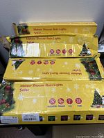 Four yellow boxes of Meteor Shower Rain Lights with Christmas tree and snowman graphics, showing severe damage to boxes from storage.