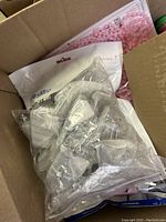 Box of small clear plastic pieces individually bagged, showing contents in transparent plastic bags.