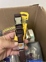 Close-up photo of a brown Carhartt adjustable dog collar with buckle and packaging tag in a box with other miscellaneous items.
