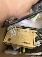 Photo showing Bestek box and coiled white earphones in plastic bag with other miscellaneous items under hand holding cord.