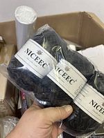 Hand holding skeins of NICEEC chunky black yarn in the box of miscellaneous items.