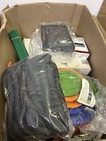 Top view of box showing green garden stakes upright and multiple coiled hoses along with black electronic device in plastic wrap.