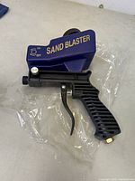 Photo showing full sandblaster tool including blue sand container, black handle, trigger, and connection fitting.