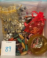 Box of assorted costume jewelry including necklaces, rings, earrings, and brooches with small fabric bags containing items for organization.