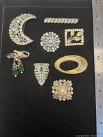 Top view of all 8 brooches arranged flat on black background with ruler for size reference