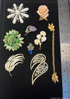 Brooch lot viewed from front, showing all brooches and sweater clip with ruler for size reference