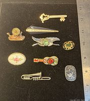 Top view of 9 brooches arranged on black background showing shapes, colors, and relative sizes alongside ruler for scale.