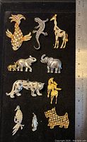 Full lot photo with ruler showing all 10 brooches including fish, lizard, giraffe, elephants, leopard, horse, parrot, penguin and dog.