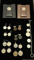 Full lot of coin accessories arranged on black background: two leather card holders, multiple pairs of earrings, cufflinks, pendants, and a coin bracelet.