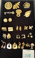 Full view of the costume jewelry lot showing multiple gold-tone brooches, pins, and earrings on black display board.