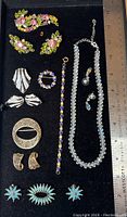 Overview of the first set of costume jewelry with colorful rhinestone brooches, earrings, bracelet, and clear bead necklace, placed on black velvet under a ruler showing about 7 inches in length.