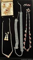Four jewelry sets displayed on a black surface showing brooch with earrings in original box and multiple silver-tone rhinestone necklaces and bracelets