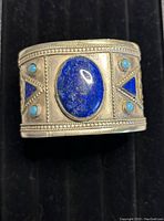 Front view showing large oval lapis lazuli cabochon center stone flanked by smaller turquoise stones and triangular lapis inlays. Metal surface has intricate rope-like border detail.