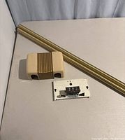 Set of mid-century modern doorbell button, chime mechanism, and gold trim piece on table