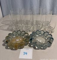 Full view of 8 clear Imperial Candlewick tumblers and 2 bubble bead ashtrays on table.