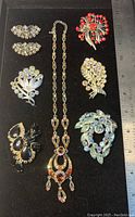 Top view of 7 pieces of vintage AB rhinestone jewelry arranged on black velvet with a ruler for size reference