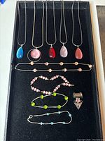 Top-down image of the jewelry lot with necklaces and bracelets displayed on black fabric with a ruler for scale.