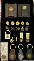 Display of two leather credit card holders in brown and black, multiple round pendants, key chains including leather fob attachments, money clips, and cufflinks all featuring New York City transportation token designs.