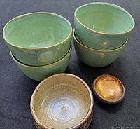 Photo showing 4 green bowls stacked in two pairs, 1 brown bowl, and 1 small gold gilt dish placed in front.