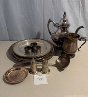 Full view of the silver-plated collection including plates, teapot, cream pitcher, napkin holders, ladle, and salt and pepper shakers arranged on table.