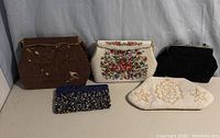 Five beaded purses arranged against a white backdrop, showing front details and design variety including brown, white floral, black, white beaded star design, and multicolored modern purse.