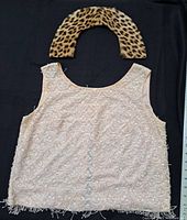 Front view of pink sequined sleeveless blouse alongside cheetah print fur collar placed above it on black background with measuring tape for scale.