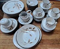 Overview of the full set including plates, bowls, cups, saucers, and serving pieces, showing the brown wheat stalk decoration on ceramic.
