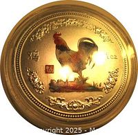 Obverse of round gold-colored China token featuring a colored rooster, floral patterns, and 1 oz weight marking