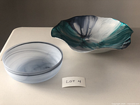 Two decorative bowls displayed side by side on a white surface. The larger bowl is fluted, multi-toned with blue and green shades, approx. 14 inches in diameter. The smaller bowl is round with soft blue-grey swirls, approx. 8.25 inches in diameter.