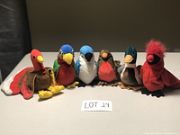 Photo showing 6 bird plushies including a red turkey, green/red parrot, bluejay, robin, duck-like drake, and red cardinal.