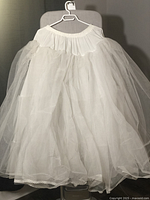 Full view of the white crinoline skirt hanging on a chair, showing its volume and length.