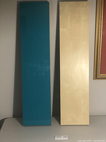 Two rectangular floating shelves standing vertically side by side; one is a natural light wood color, the other is turquoise blue.