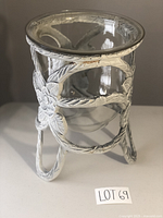 Front view of the decorative metal stand holding the glass urn with floral and rope design painted white, showing rust spots.