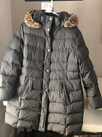 Front view of the women's nylon winter coat showing the snap-button storm flap, two zippered pockets with snap closures, and the hood with brown faux fur trim.
