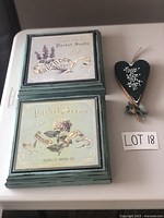 Photo showing two square wooden wall hangings with vintage seed packet illustrations for Lavender and Hydrangea, plus a black heart-shaped wall hanging with text and ribbon.