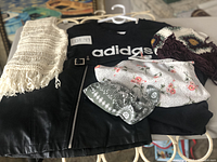 Photo showing the black Adidas t-shirt with logo, black pleather mini skirt with front zipper and belt, white crochet knit item, floral bikini top and covers, and patterned knit items arranged flat on a glass surface.