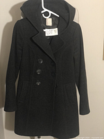 Front view of dark gray wool coat hanging on a hanger showing button double-breasted front, collar, and hood.