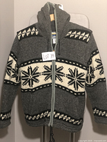 Front view of gray hooded wool coat with white and black Nordic pattern and zipper closure hung on a chair.