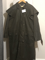 Front view of full-length coat on hanger showing cape overlay, snap closures and flap pockets