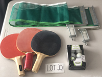 Photo showing 3 ping-pong paddles, 6 balls in box, and folded net with clamps on a white surface.