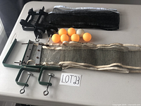 Photo showing two ping-pong nets with clamps and seven ping-pong balls, six orange and one white.