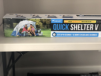 Photo of the box front showing the Light Speed Quick Shelter V tent branding with an image of a family under the tent outdoors and UPF 50+ sun protection highlighted.