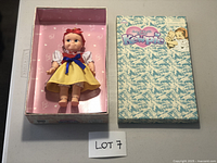 Photo showing the Kewpie doll seated in its open box, dressed in yellow, white, blue, and red outfit, labeled lot 7.