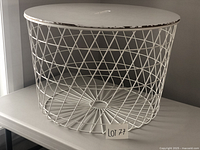 White round metal wire storage table showing wear around the edges of the wooden top, front angle view